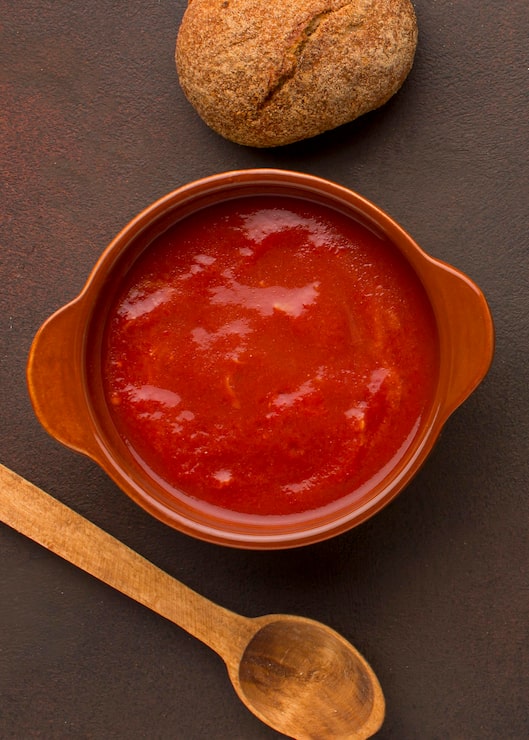 Foto gratuito vista superior de la sopa de tomate de invierno en un tazón con pan y cuchara