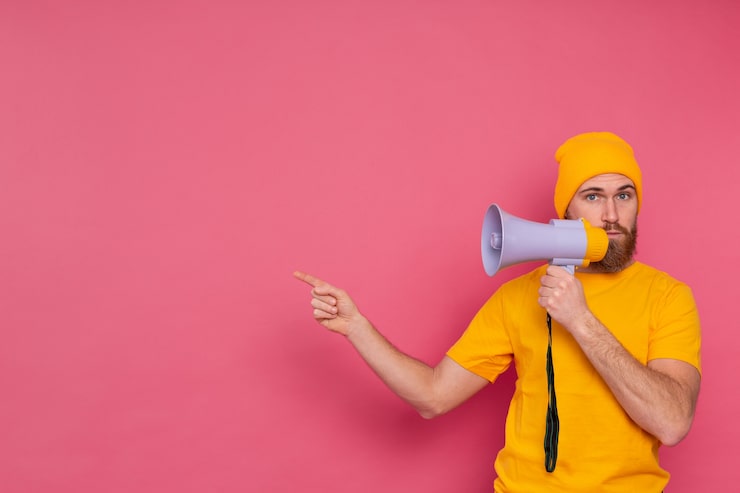 Foto gratuito attenzione! uomo europeo con il megafono che punta il dito a sinistra su sfondo rosa