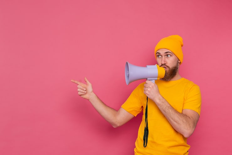 Foto gratuito attenzione! uomo europeo con il megafono che punta il dito a sinistra su sfondo rosa