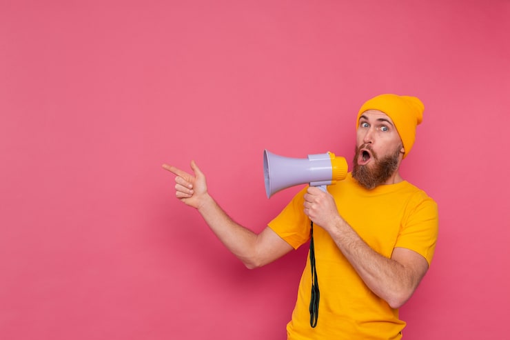Foto gratuito attenzione! uomo europeo con il megafono che punta il dito a sinistra su sfondo rosa