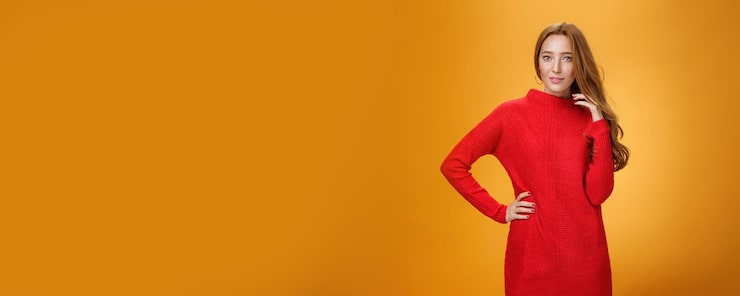 Foto gratuito attraente donna rossa sensuale e romantica in abito elegante lavorato a maglia rosso che tiene la mano sull'anca smili