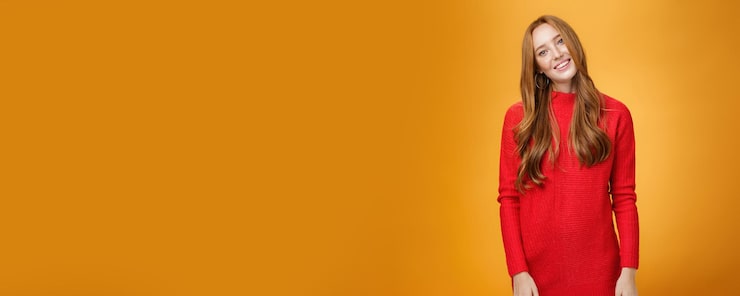 Foto gratuito busiensswoman elegante attraente ed alla moda con capelli rossi in vestito lavorato a maglia rosso che inclina testa e s