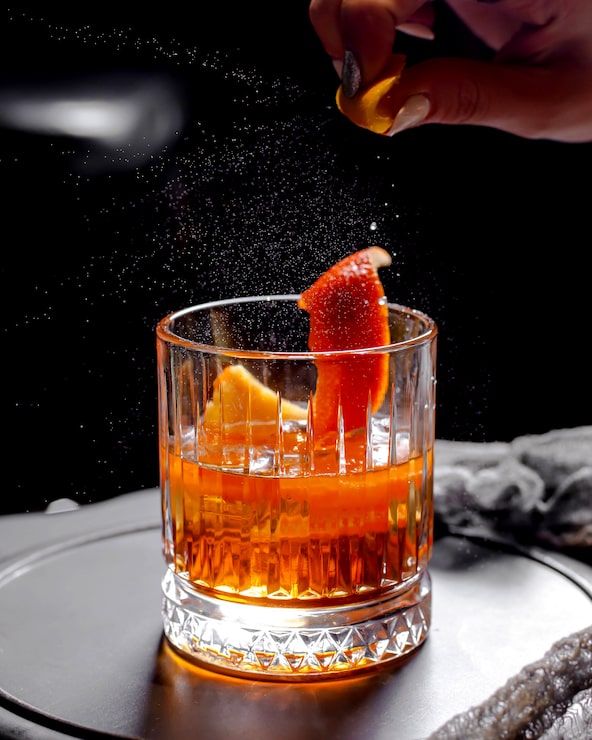 Foto gratuito close up di bicchiere di whisky di cristallo con cocktail alcolico guarnito con crosta d'arancia