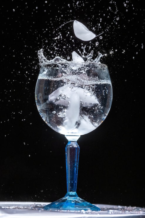 Foto gratuito colpo verticale del primo piano di un bicchiere di acqua ghiacciata con spruzzi