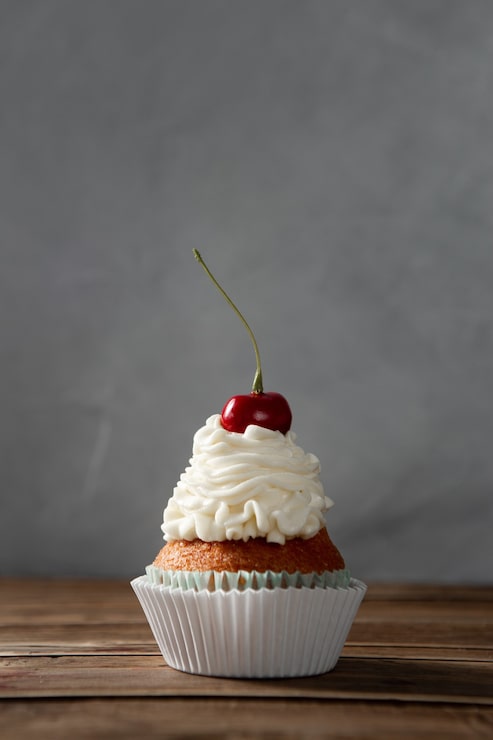 Foto gratuito colpo verticale di un delizioso cupcake con panna e ciliegina sulla torta