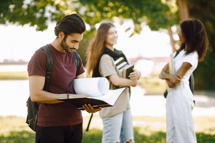 Foto gratuito concentrati su un ragazzo indiano che sta in piedi separatamente. gruppo di studenti internazionali in piedi insieme nel parco dell'università