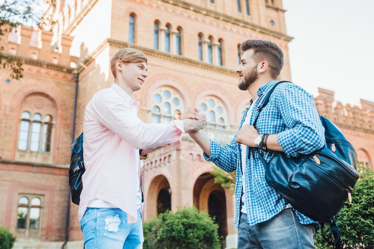 Foto gratuito due giovani bei ragazzi di studenti con zaini si salutano al campus. all'università.