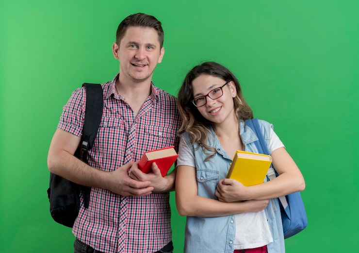 Foto gratuito giovane coppia uomo e donna in abiti casual con zaini in possesso di libri sorridente amichevole in piedi sopra la parete verde