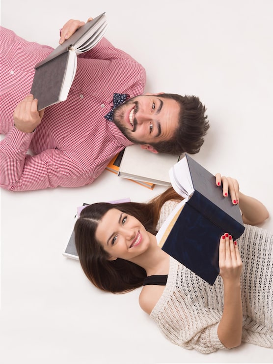 Foto gratuito giovani coppie di studenti sdraiati per terra, che leggono libri e sorridono felici per la cmera. persone sdraiate una accanto all'altra.