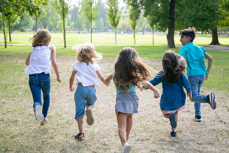 Foto gratuito gruppo di ragazzi che corrono insieme sull'erba, avendo corsa nel parco. vista posteriore, a figura intera. concetto di attività all'aperto per bambini