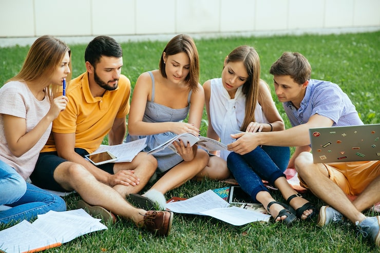 Foto gratuito gruppo di studenti che studiano seduti sull'erba con i quaderni