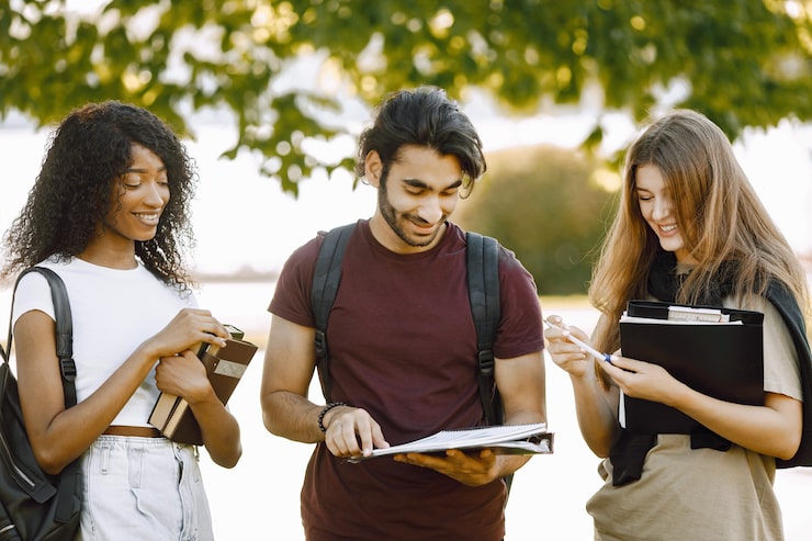 Foto gratuito gruppo di studenti internazionali in piedi insieme nel parco all'università. ragazze africane e caucasiche e ragazzo indiano che parlano all'aperto