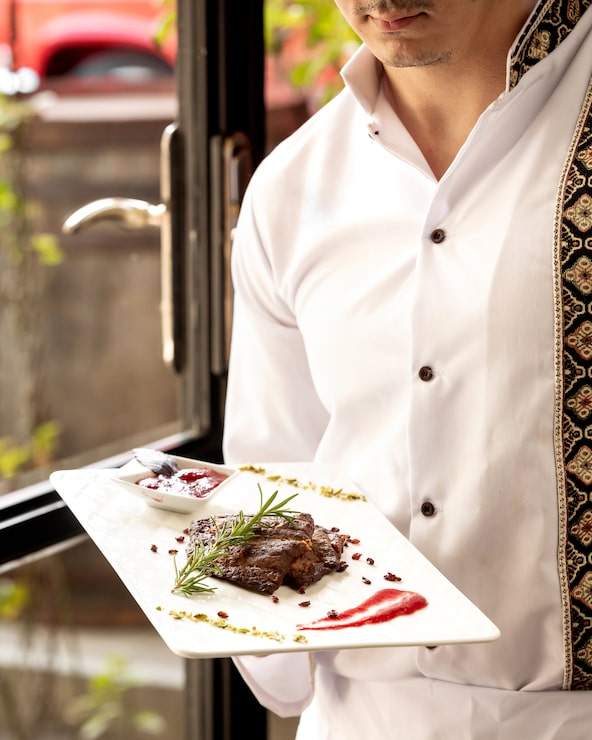 Foto gratuito il cameriere che tiene un piatto di pezzi di bistecca è servito con salsa acida