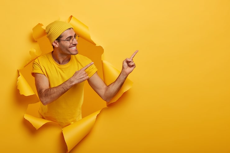 Foto gratuito il modello maschile europeo positivo punta a destra con entrambi gli indici, suggerisce di utilizzare il prodotto, si gira di lato