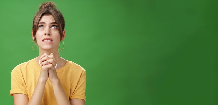 Foto gratuito intensa giovane donna dall'aspetto nervoso e fedele che stringe le mani insieme sul petto guardando in alto