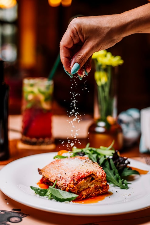 Foto gratuito la donna spruzza le particelle di parmigiano grattugiate sulle lasagne
