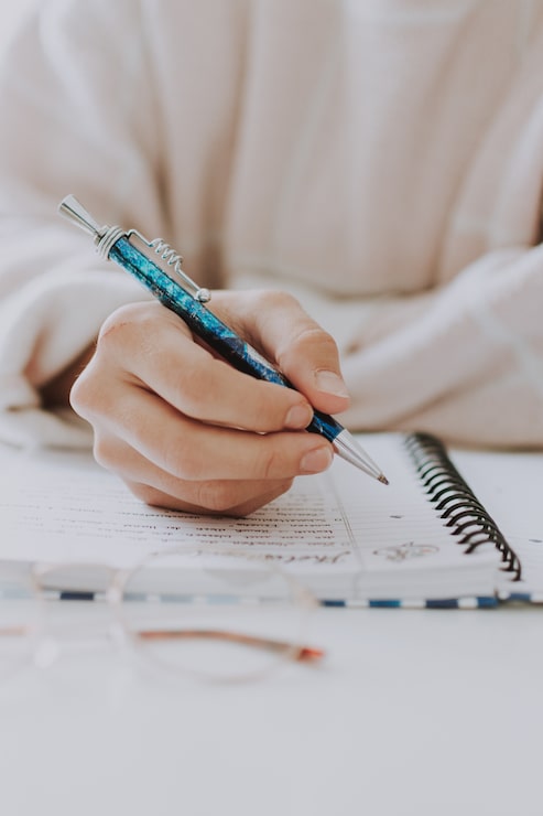 Foto gratuito prossimo piano verticale selettivo di una donna che scrive in un quaderno con una penna blu