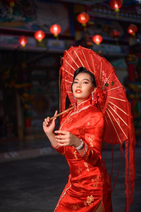 Foto gratuito scena notturna, ritratto asian bella donna che indossa un cheongsam sorridente e posa con carta ombrello rosso al santuario il capodanno cinese