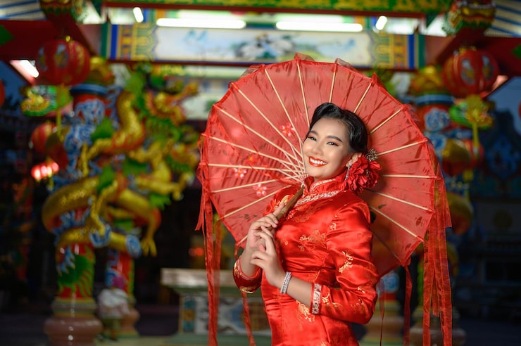 Foto gratuito scena notturna, ritratto asian bella donna che indossa un cheongsam sorridente e posa con carta ombrello rosso al santuario il capodanno cinese