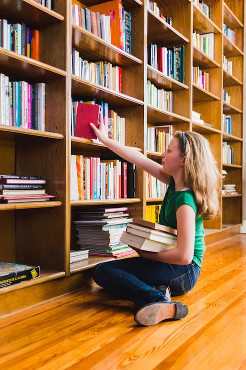Foto gratuito sedendosi sulla ragazza del pavimento che mette libro sullo scaffale