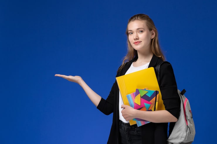 Foto gratuito studentessa di vista frontale in camicia bianca e giacca nera che indossa lo zaino che tiene i file con i quaderni sulle lezioni dell'università dell'università della parete blu
