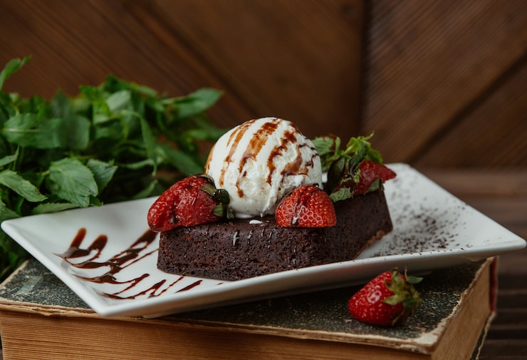 Foto gratuito un brownie al cioccolato servito con una palla di gelato alla vaniglia e fragole