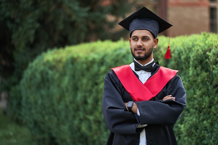 Foto gratuito un laureato indiano serio in abito da laurea con le braccia incrociate che guarda avanti.