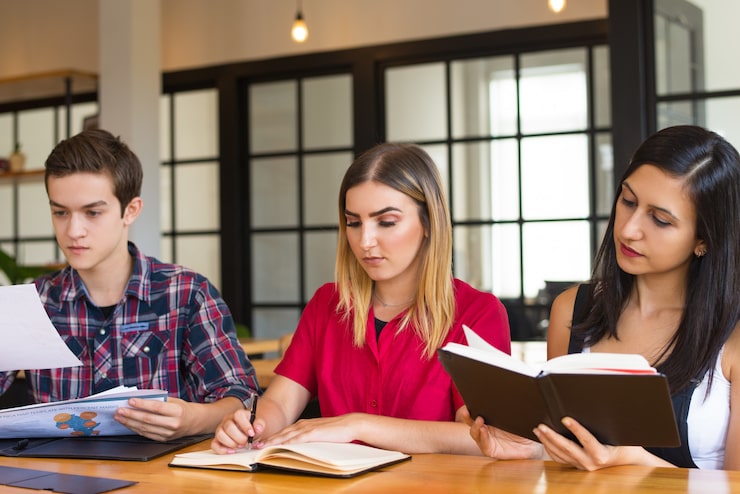 Foto gratuito un ritratto di tre studenti seri che studiano nella biblioteca