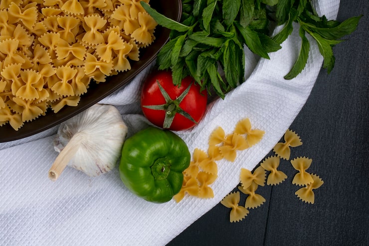 Foto gratuito vista dall'alto di pasta cruda in una ciotola con pomodori aglio e peperoni con menta su un asciugamano bianco su una superficie nera