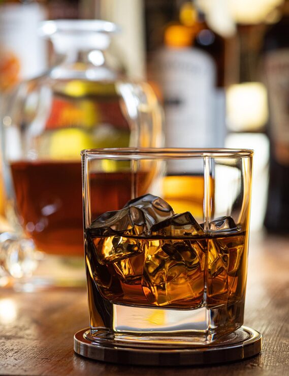 Foto bicchiere di whisky sulle rocce su un piano bar in legno con bottiglie sullo sfondo