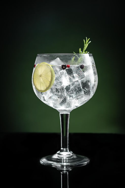 Foto bicchiere freddo di gin tonic con ghiaccio su sfondo verde scuro con spazio per la copia formato verticale