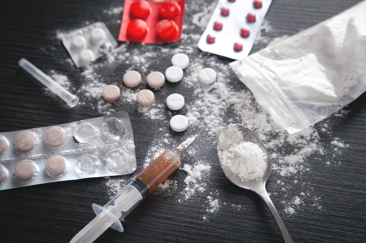 Photo bubuk heroin, pil, dan jarum suntik di latar belakang gelap.