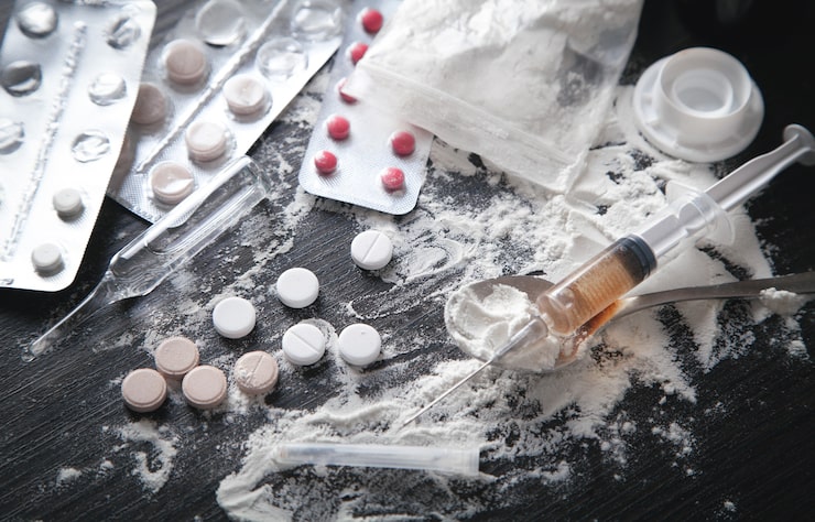Photo bubuk heroin, pil, dan jarum suntik di latar belakang gelap.