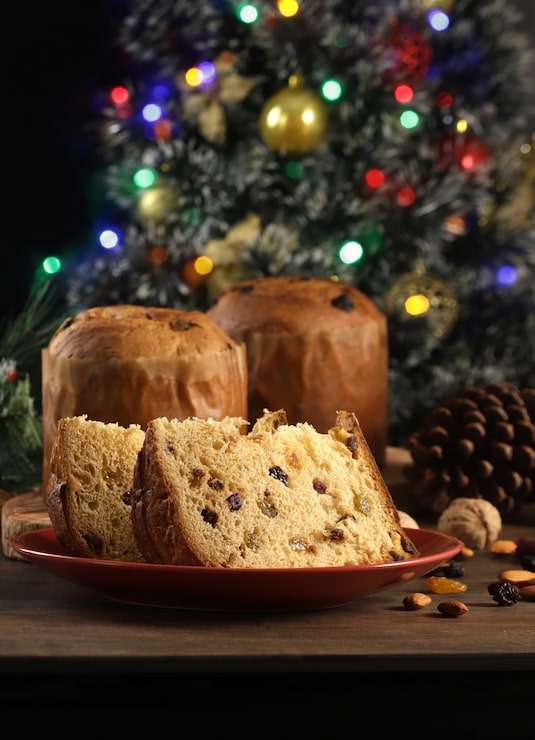 Foto deliziosa fetta di panettone con frutta candita sul tavolo su uno sfondo sfocato.