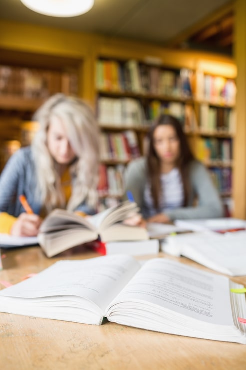 Foto due studenti offuscati che scrivono le note allo scrittorio della biblioteca