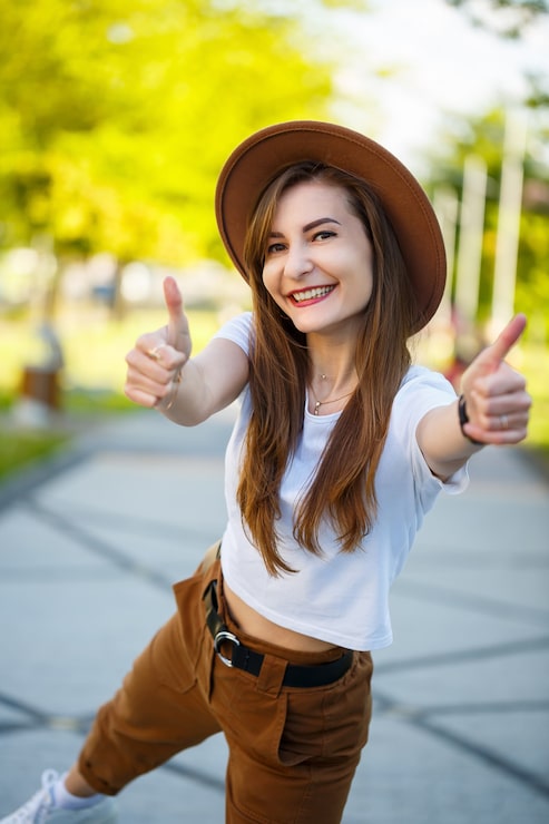 Photo gadis berambut cokelat tertawa dengan kulit pucat mengenakan pakaian trendi berdiri di taman menikmati pagi yang cerah. potret wanita muda yang sangat cantik bertopi dan t-shirt putih berpose di dekat jalan setapak taman.