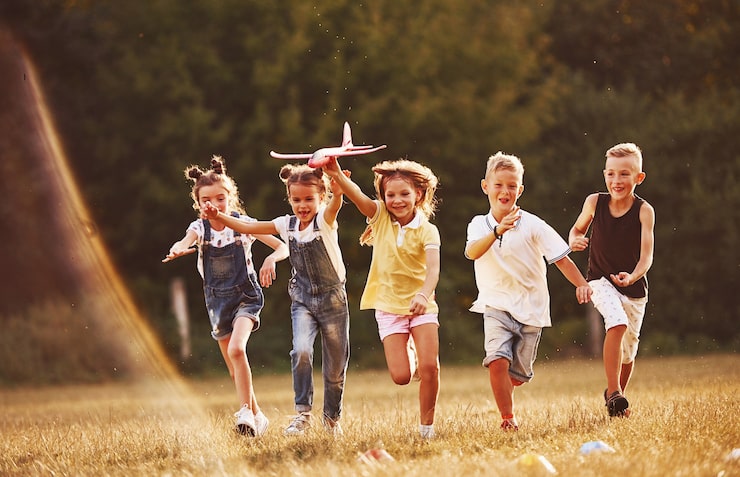 Foto gruppo di bambini che si divertono all'aperto con aeroplano giocattolo rosso nelle mani.