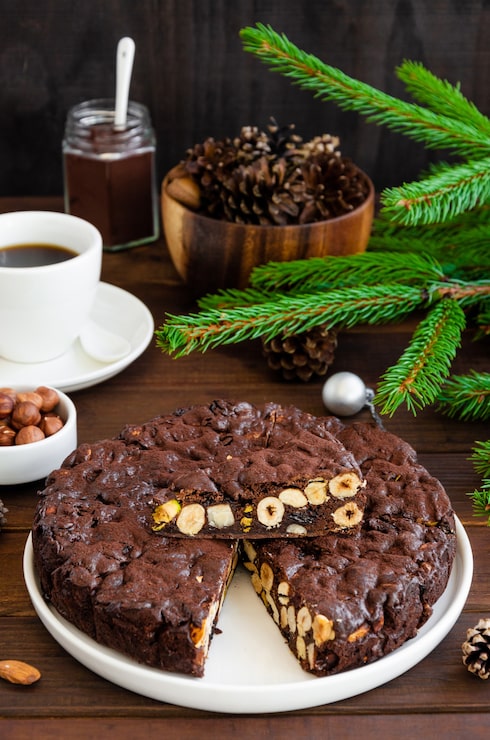 Foto panforte. dolce natalizio italiano tradizionale con noci e frutta secca su un piatto bianco su un fondo di legno scuro. verticale, copia spazio.