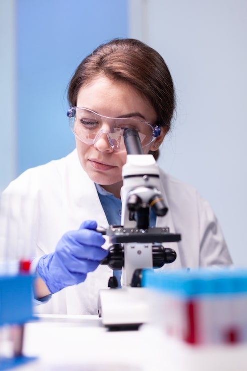 Foto grátis cientista caucasiana de jaleco branco olhando em um microscópio de última geração para obter experiência em farmácia