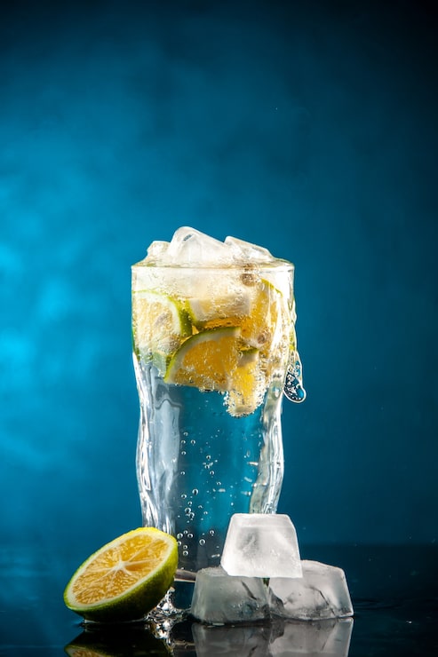 Foto grátis copo de refrigerante com rodelas de limão e cubos de gelo em uma foto azul champanhe coquetel de água com limonada