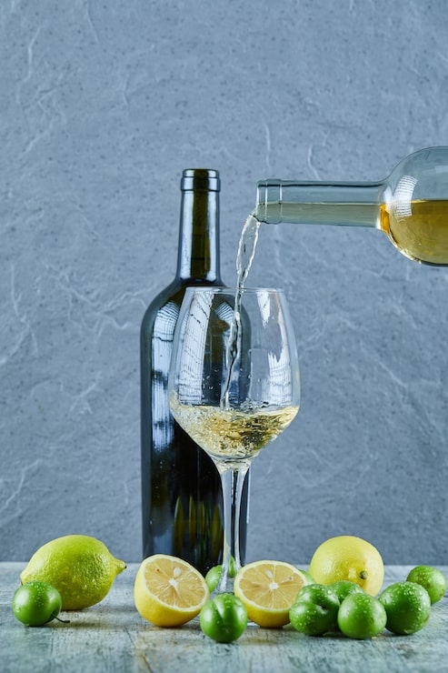 Foto grátis derramando vinho branco no copo e limões, garrafa de vinho e ameixas de cereja de lado