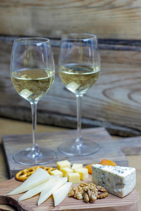 Foto grátis dois copo de vinho branco com tábua de queijos no rústico com vários queijos, queijo azul, gauda e nozes e lanches