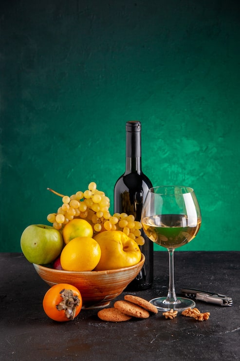 Foto grátis frente frutas frescas em uma tigela maçã marmelo uvas limão garrafa de vinho de caqui e biscoitos de vidro abridor de vinho na mesa verde