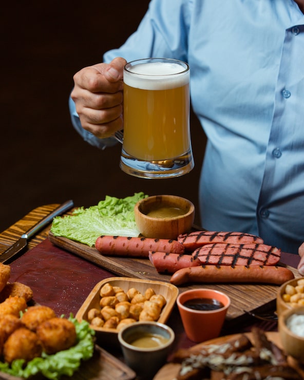 Foto grátis homem segurando a caneca de cerveja servida com salsichas grelhadas, grão de bico, almôndegas crocantes