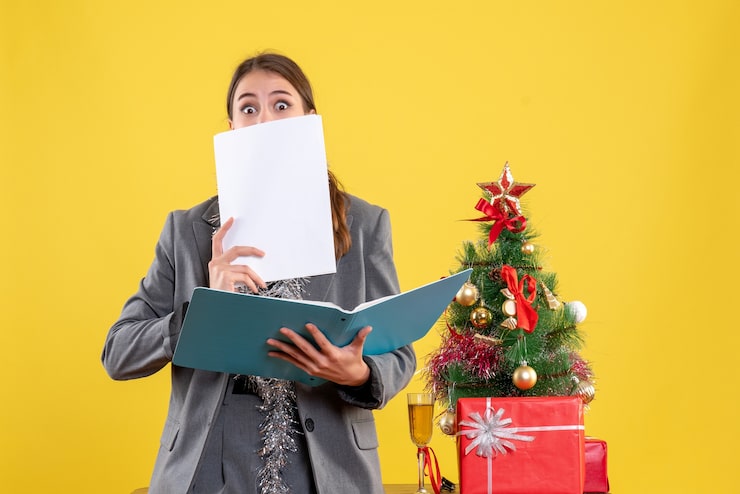 Foto grátis jovem de olhos arregalados de frente verificando documentos em pé perto da árvore de natal e coquetel de presentes