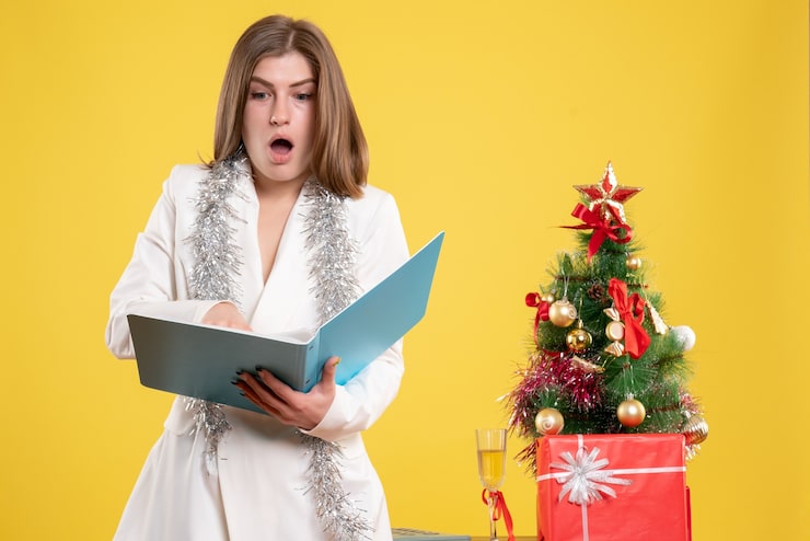 Foto grátis médica de frente, de pé, segurando documentos em fundo amarelo com árvore de natal e caixas de presente