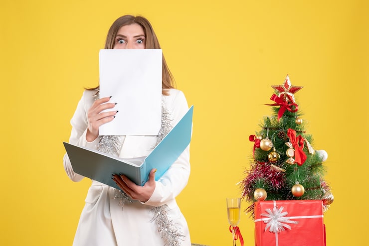 Foto grátis médica de frente, de pé, segurando documentos em fundo amarelo com árvore de natal e caixas de presente