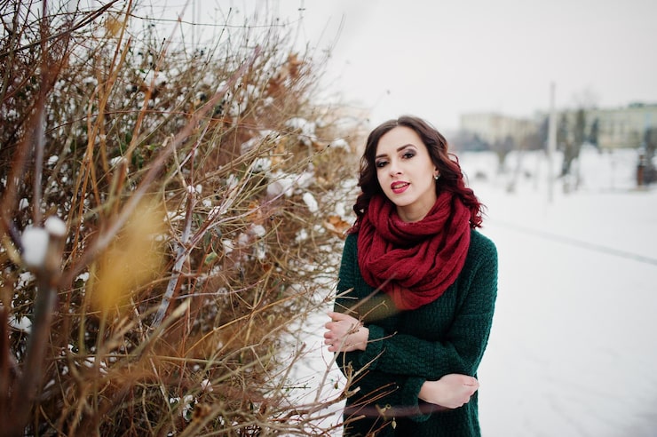 Foto grátis menina morena de suéter verde e lenço vermelho ao ar livre contra arbustos na noite de inverno