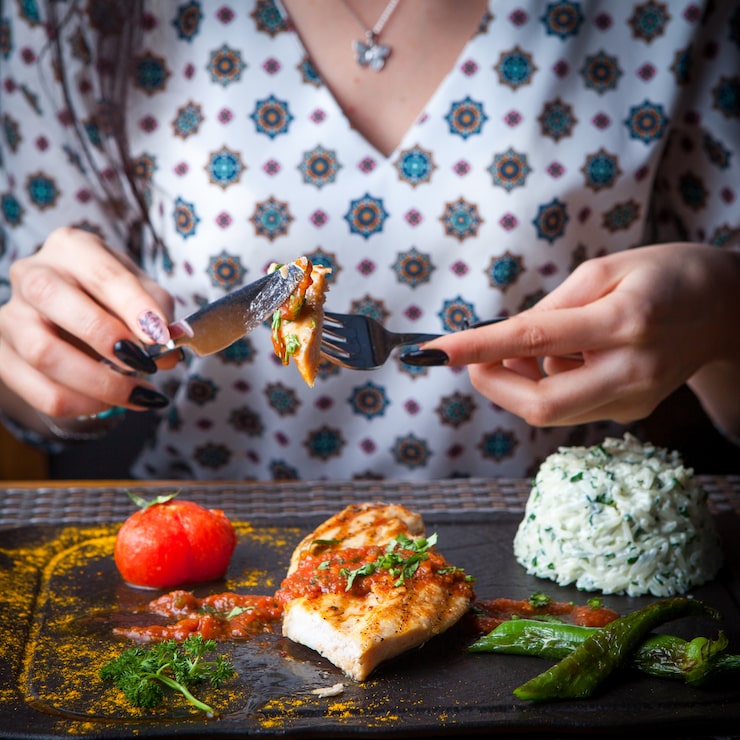 Foto grátis mulher de bife de frango grelhado close-up come com uma faca e garfo com enfeite, tomate, pimenta uma mesa de madeira escura horizontal