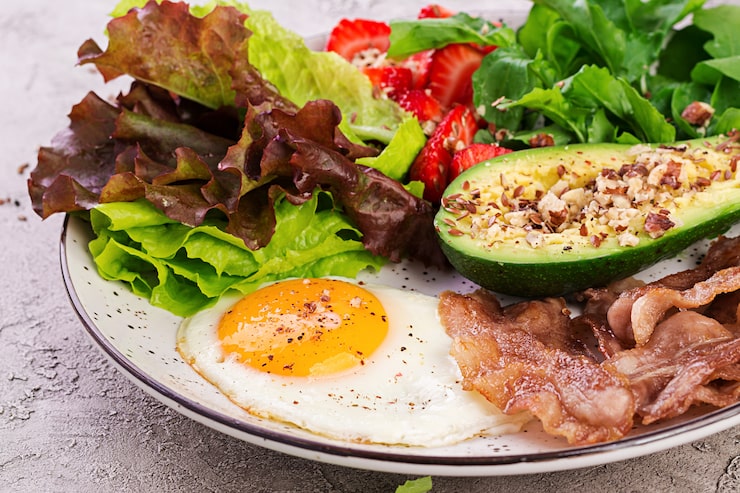 Foto grátis prato com um alimento de dieta ceto. ovo frito, bacon, abacate, rúcula e morangos. keto café da manhã.